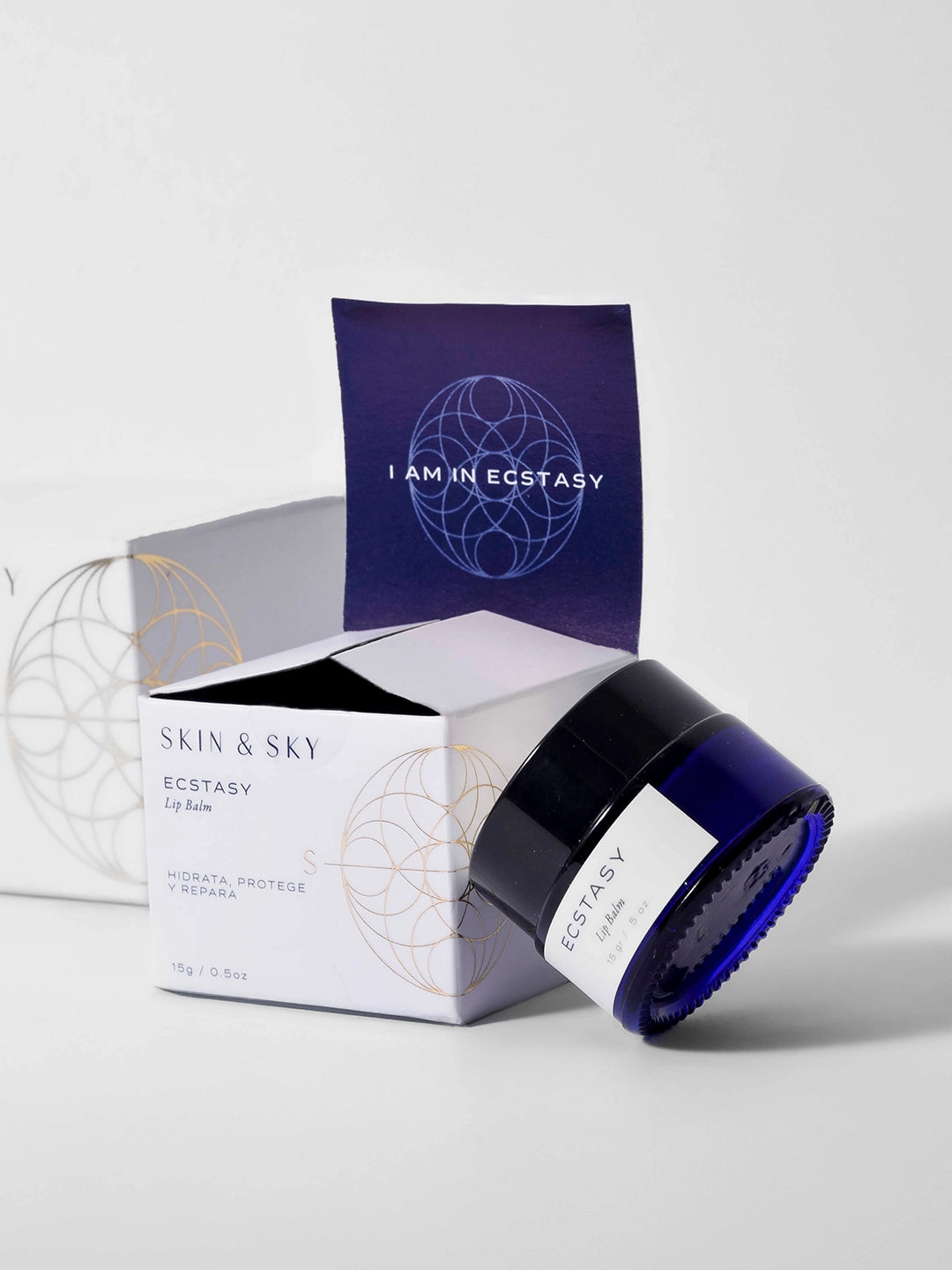 Bálsamo labial Ecstasy de Skin & Sky en tarro de vidrio azul con caja blanca; fórmula de 15g diseñada para hidratar, proteger y reparar labios secos.