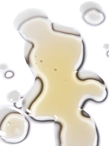 Muestra de la textura del aceite corporal Abundance de Skin & Sky; gotas de aceite dorado translúcido con burbujas de aire sobre un fondo blanco limpio y brillante.