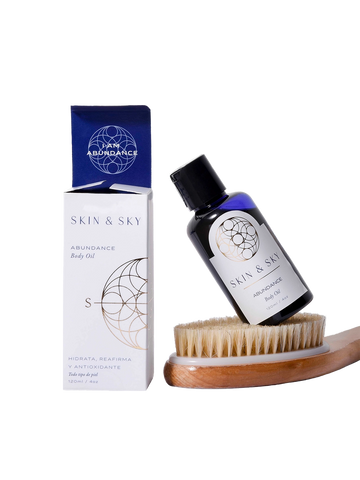 Set Body Duo de Skin & Sky que incluye el aceite corporal Abundance de 120ml apoyado sobre un cepillo de cerdas naturales para exfoliación en seco, junto a su empaque minimalista blanco y azul.