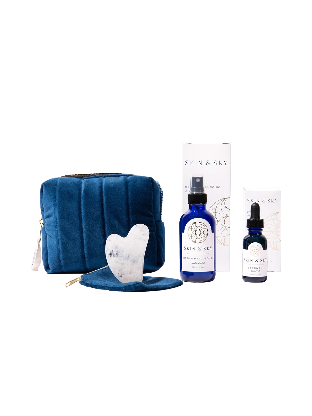 Eternity Set de Skin & Sky: incluye el Eternal Facial Oil (30ml), Rose & Hyaluronic Radiant Mist (120ml), una Gua Sha de cuarzo blanco con su funda protectora y una cosmetiquera de terciopelo azul marino, presentados con sus cajas de empaque minimalistas.