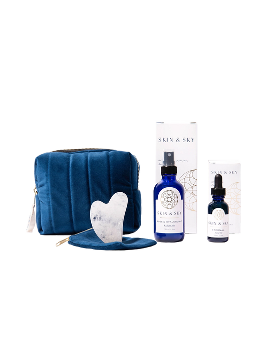 Eternity Set de Skin & Sky: incluye el Eternal Facial Oil (30ml), Rose & Hyaluronic Radiant Mist (120ml), una Gua Sha de cuarzo blanco con su funda protectora y una cosmetiquera de terciopelo azul marino, presentados con sus cajas de empaque minimalistas.