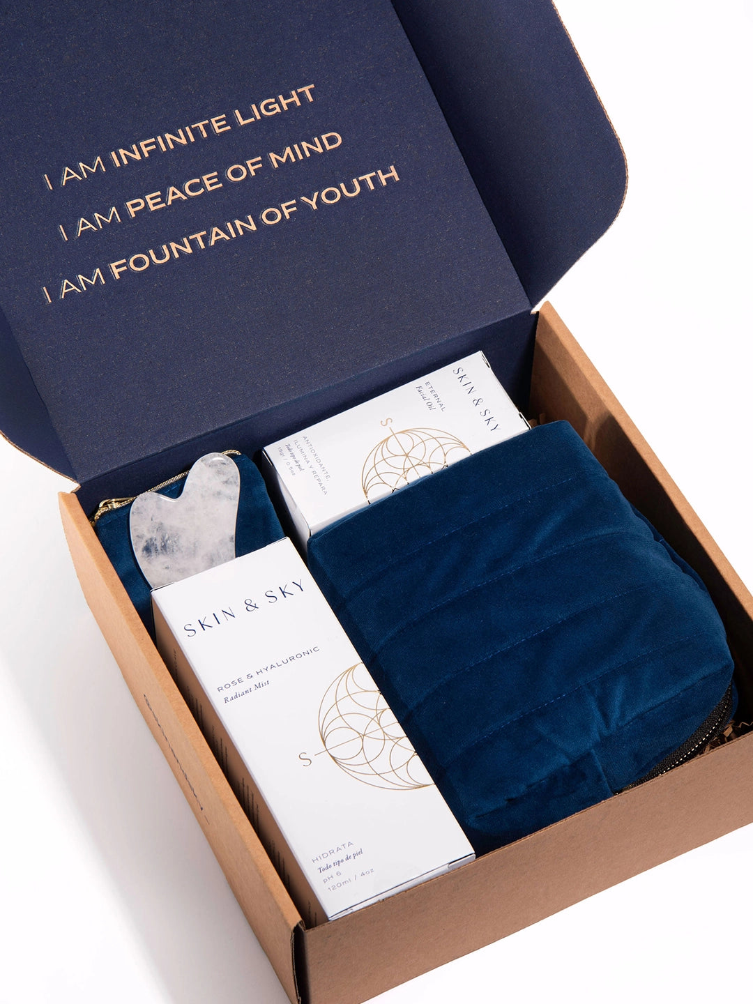 Vista interior de la caja de regalo del Eternity Set abierta, revelando los productos y una cosmetiquera azul. La tapa interior muestra las afirmaciones doradas: "I am infinite light", "I am peace of mind" e "I am fountain of youth".