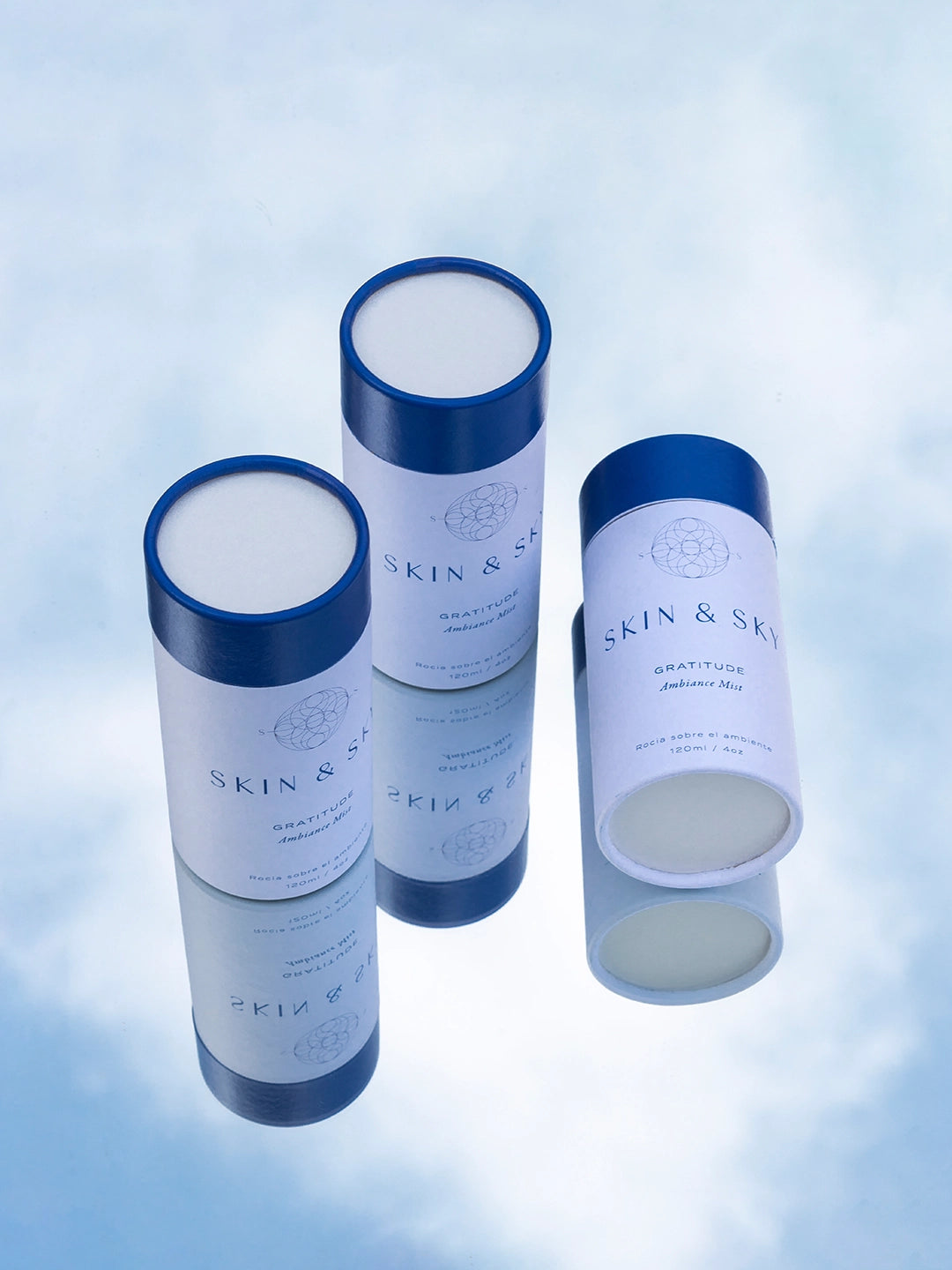 Empaque Gratitude Ambiance Mist Skin & Sky blanco con tapa azul en fondo degradado azul, bruma aromática para el ambiente con aceites esenciales, 120 ml.