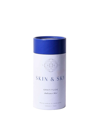 Gratitude Ambiance Mist Skin & Sky en envase cilíndrico blanco con tapa azul sostenido en manos, bruma aromática para armonizar el ambiente, 120 ml.