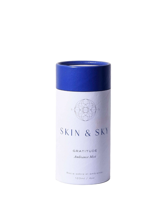 Gratitude Ambiance Mist Skin & Sky en envase cilíndrico blanco con tapa azul sostenido en manos, bruma aromática para armonizar el ambiente, 120 ml.