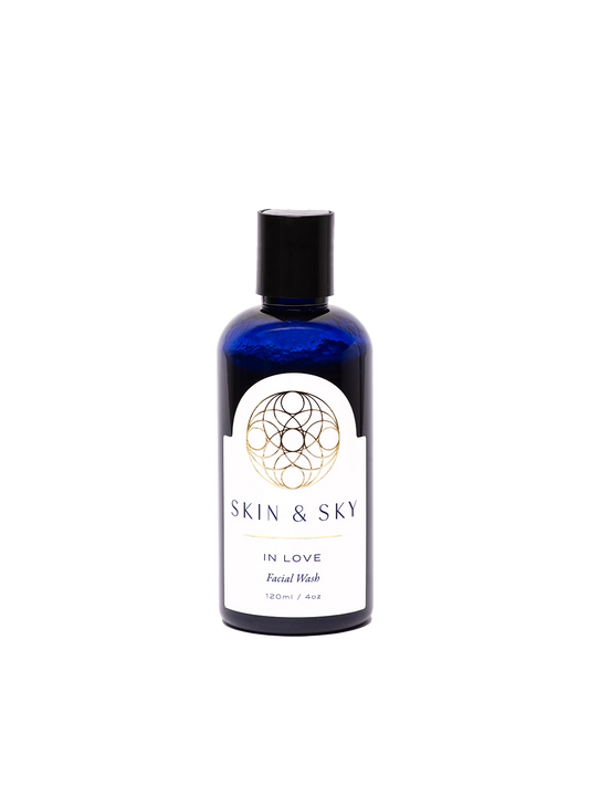 Botella azul de In Love Facial Wash de Skin & Sky, 120 ml / 4 oz. Limpieza facial hidratante y equilibrante con diseño elegante del logotipo doradao en la etiqueta. Limpia, hidrata y nutre la piel con salvia, menta, eucalipto, rosa mosqueta, granada y miel.
