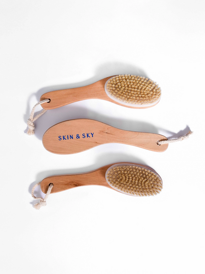 Vista aérea de tres cepillos corporales de madera con cerdas naturales y cordón de soga para colgar, dispuestos de forma organizada para mostrar el diseño ergonómico de Skin & Sky.