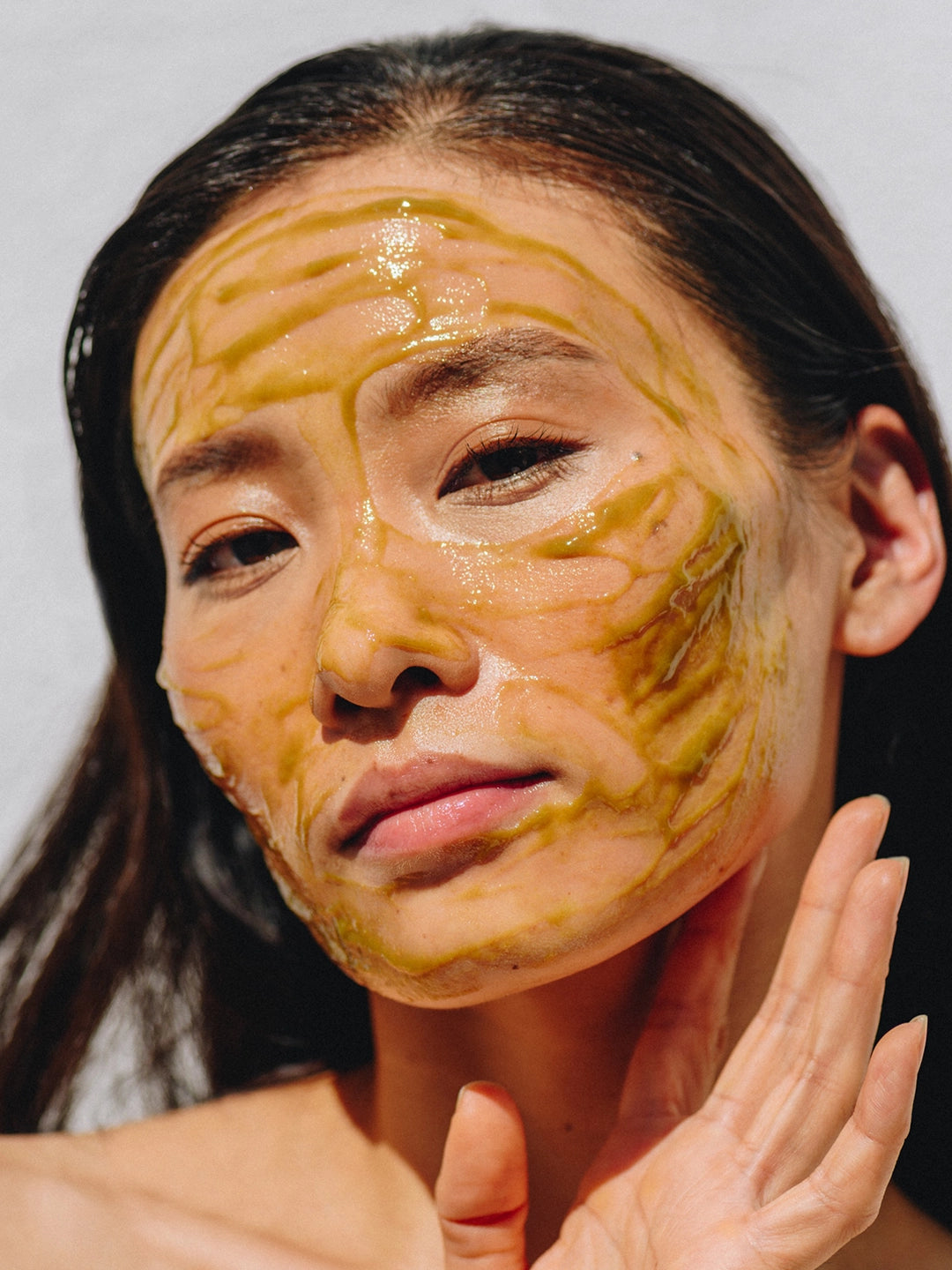 Mujer aplicando el Empower Stimulating Masque en el rostro, mostrando capas gruesas de mascarilla en tonos amarillo-verdoso brillante. Textura estimulante que rejuvenece, desintoxica y reafirma la piel con ingredientes naturales como algas y adaptógenos.