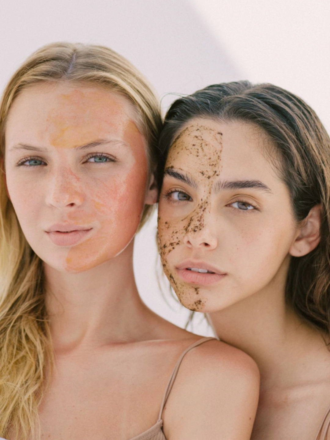 Dos modelos mostrando la aplicación de la rutina Wisdom Set; una luce la mascarilla EMPOWER de textura suave y color cálido, mientras la otra aplica el exfoliante INTUITION con partículas naturales visibles para purificar la piel.