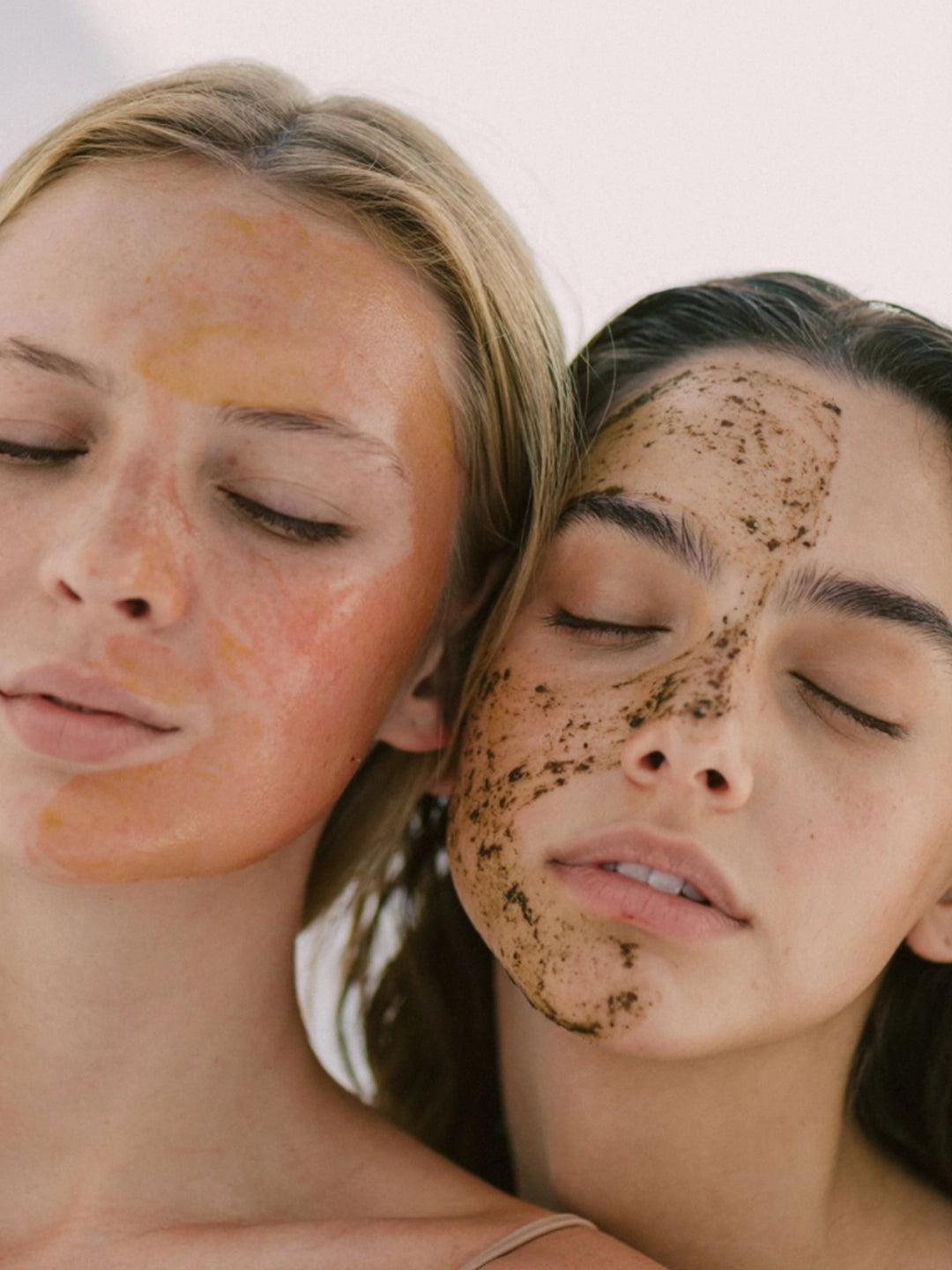 Primer plano de dos modelos con los ojos cerrados experimentando la aplicación del Wisdom Set; se aprecia la textura granulada del exfoliante INTUITION y la cobertura uniforme de la mascarilla EMPOWER para una renovación profunda.