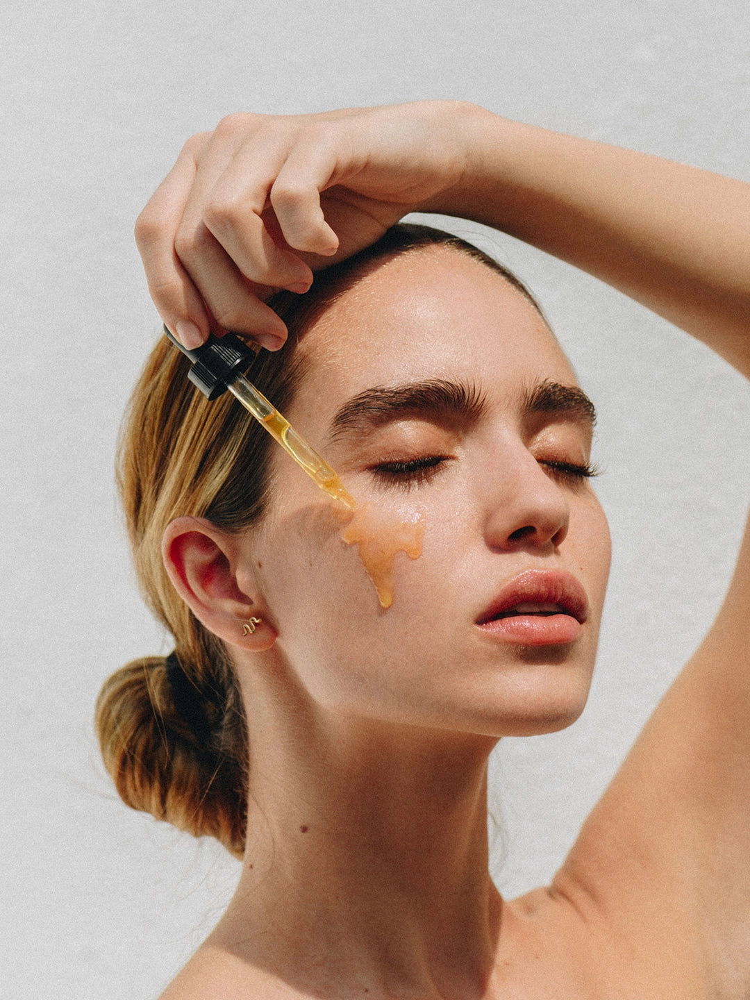 Modelo aplicando gotas de Pure Serum directamente en la mejilla, mostrando la absorción de la fórmula herbal sobre una piel limpia y radiante.