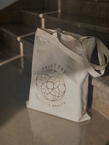 Beige tote bag with 'Skin & Sky' logo on a stone surface